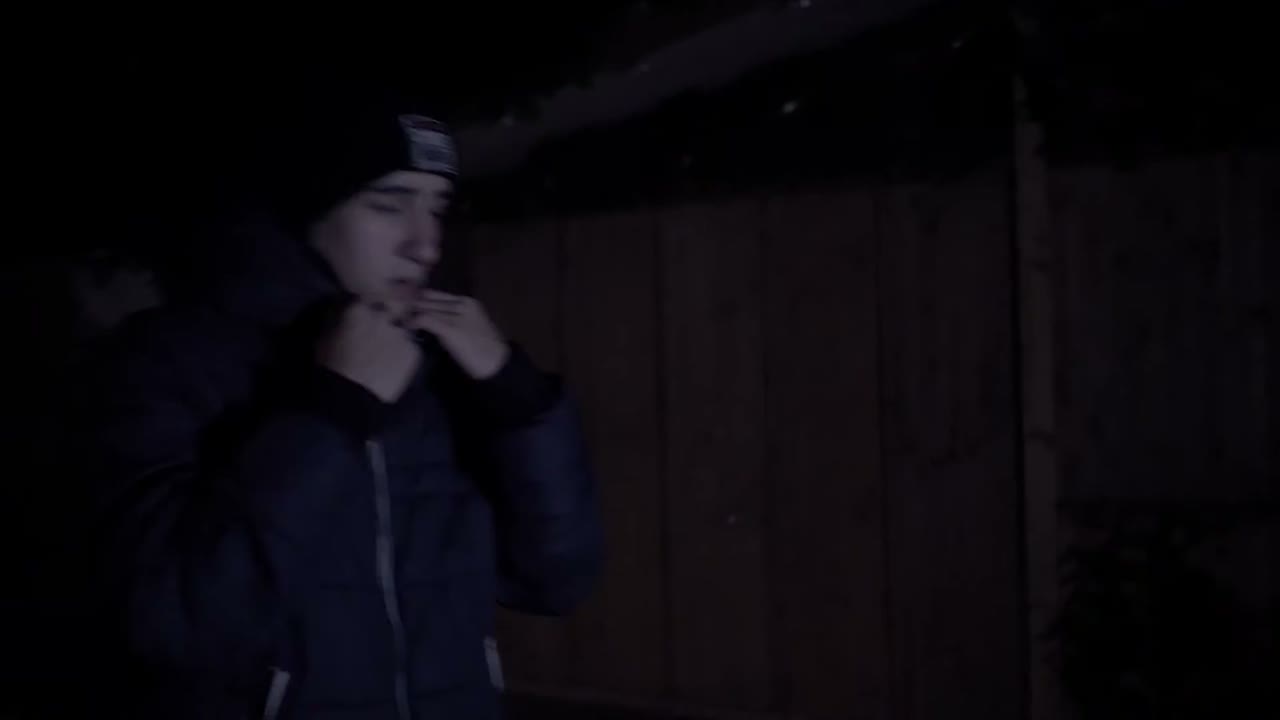 Yasin zieht im Dunkeln den Reissverschluss seiner Jacke hoch, hinter ihm eine Holzwand