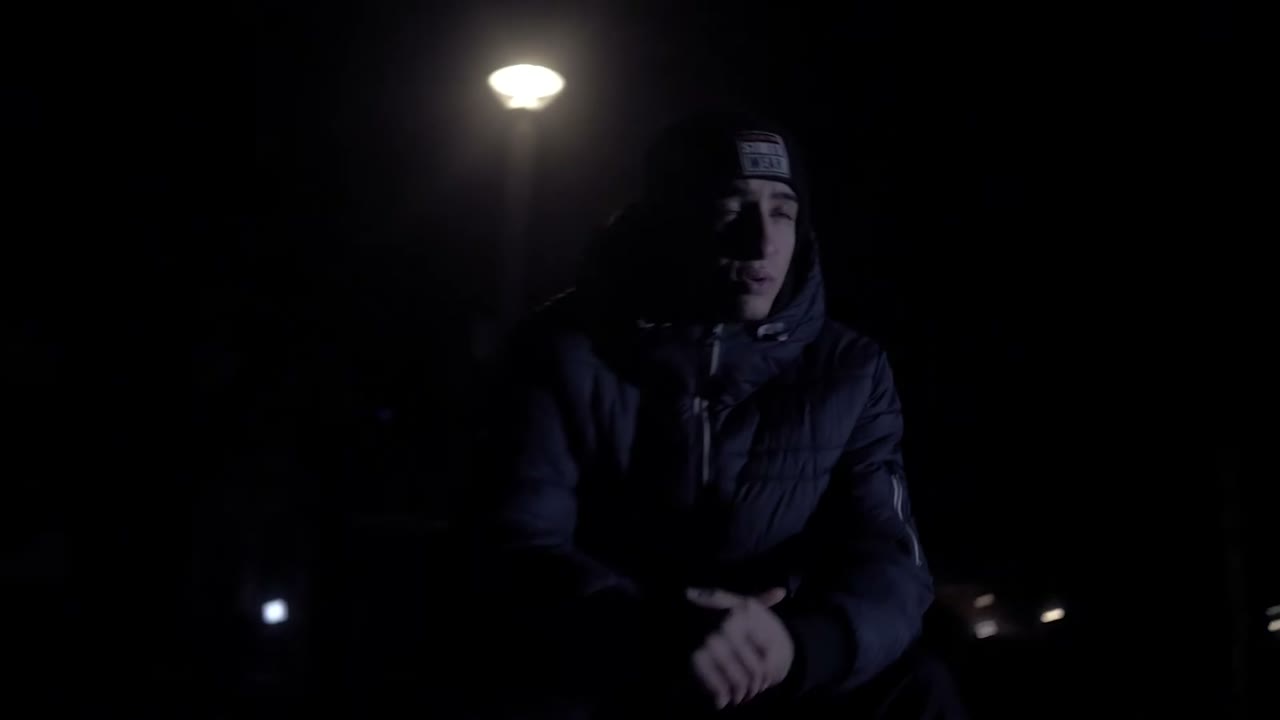 Yasin sitzt nachts unter einer Strassenlaterne