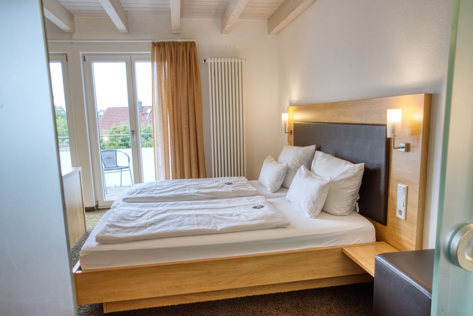 Doppelzimmer mit Holzbett, Balkontür und Blick über die Dächer