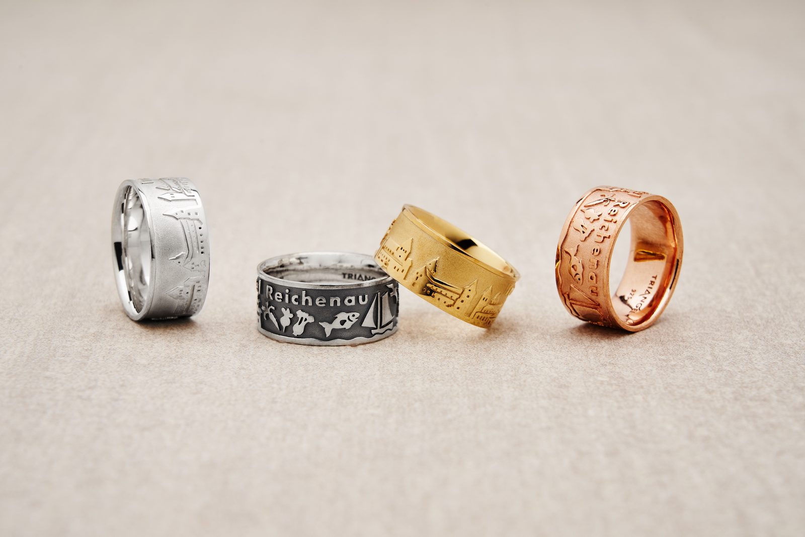 Vier Ringe in Silber, geschwärztem Silber, Gold und Roségold, graviert mit dem Schriftzug „Reichenau“, Fischen, Segelboot und Häuserzeile