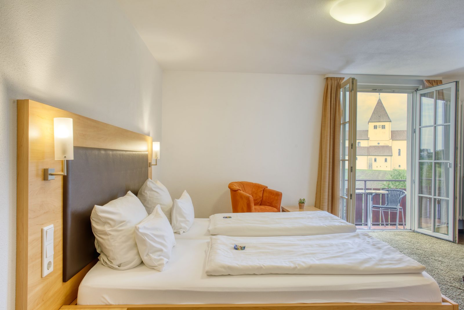 Zimmer mit offener Balkontür, dahinter der Turm der Dorfkirche