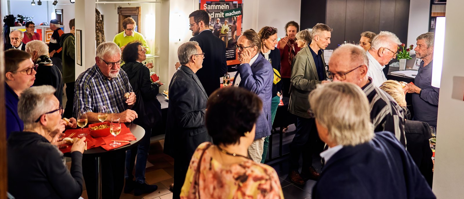 Gäste beim Apéro im Museum, im Hintergrund die Ausstellungstafeln