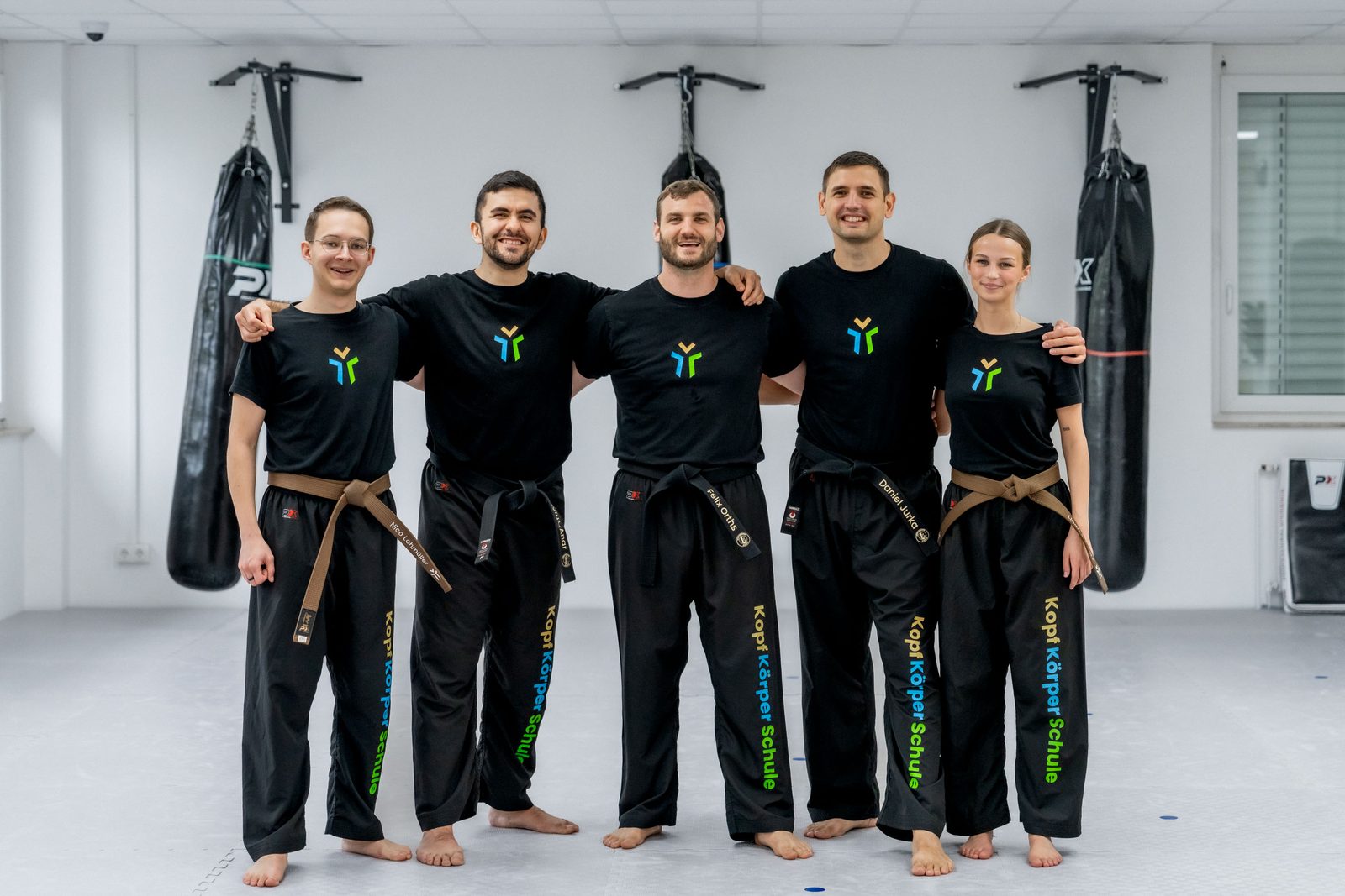 Das Team in schwarzen Anzügen vor der Reihe der Boxsäcke