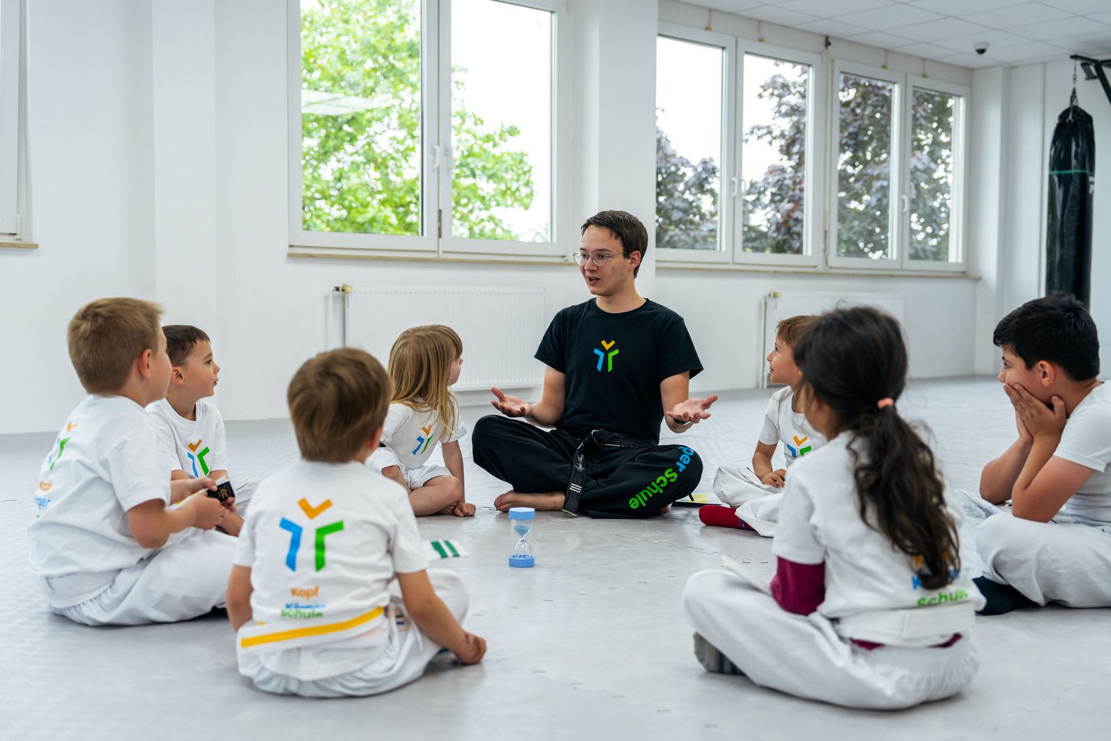Trainer sitzt mit einer Gruppe Kinder im Kreis auf dem Boden