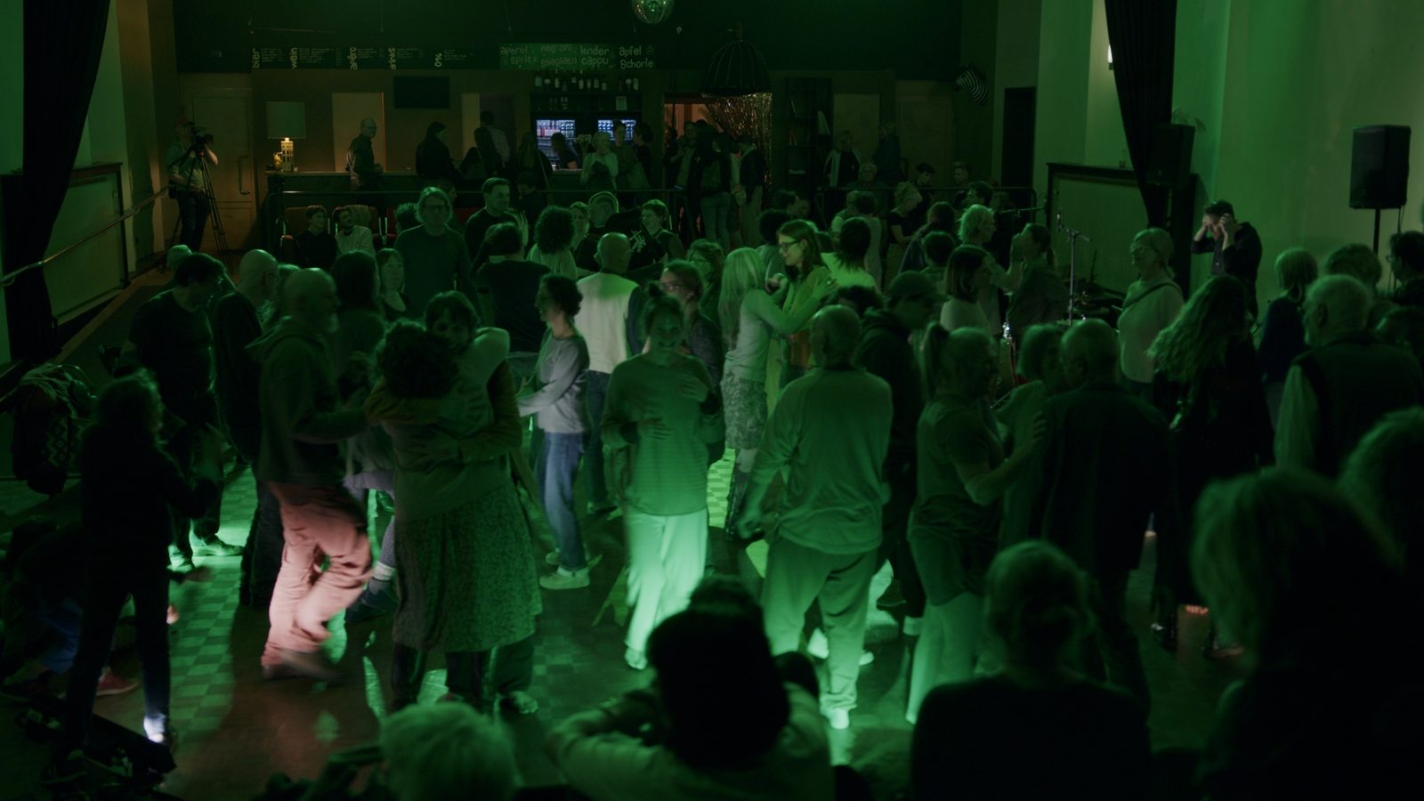 Dicht stehende Menge im grünen Licht, dahinter der dunkle Saal