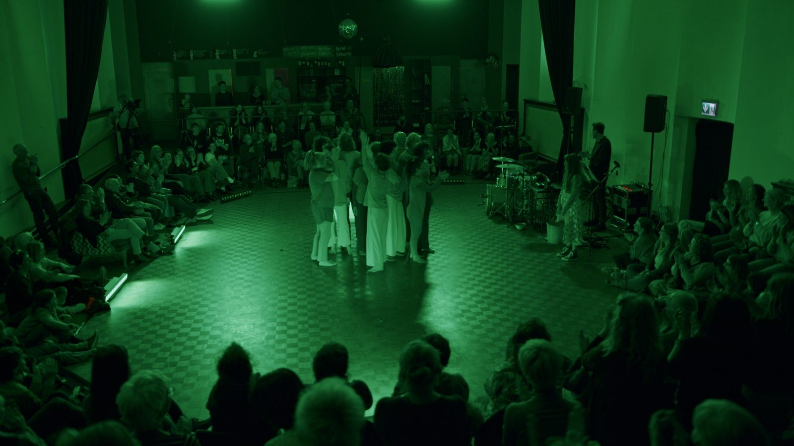 Weites rundes Lichtfeld im Saal, in der Mitte eine Gruppe, das Publikum bis an den Rand