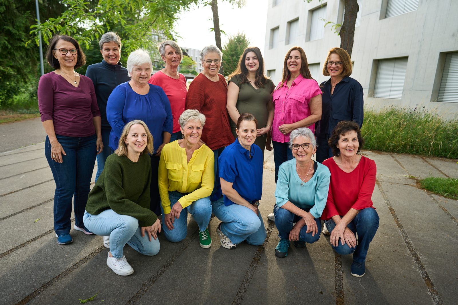 Gruppenbild: dreizehn Sängerinnen in zwei Reihen vor einer Betonwand