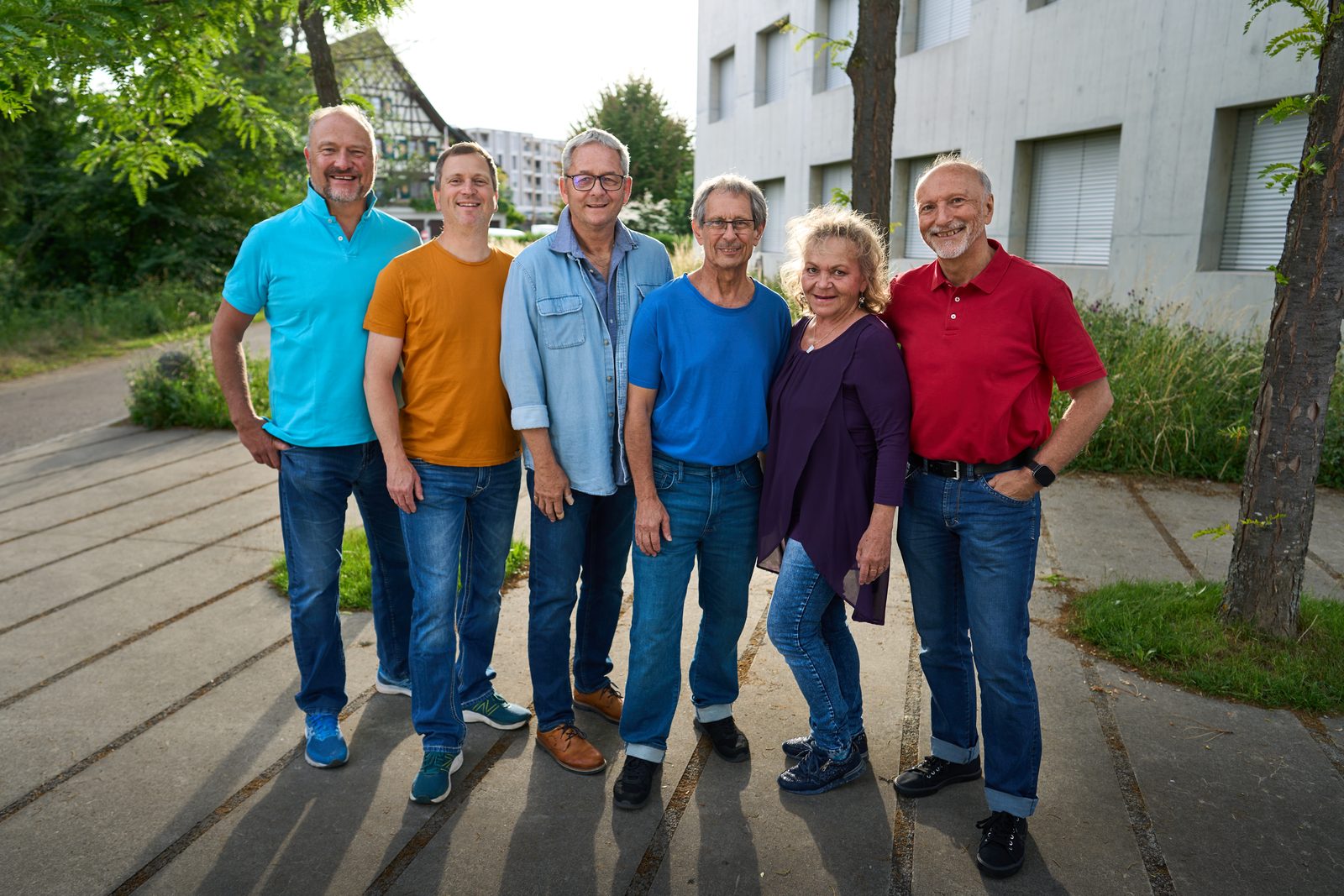 Gruppenbild: sechs Chormitglieder nebeneinander, Bäume und Betonfassade im Hintergrund
