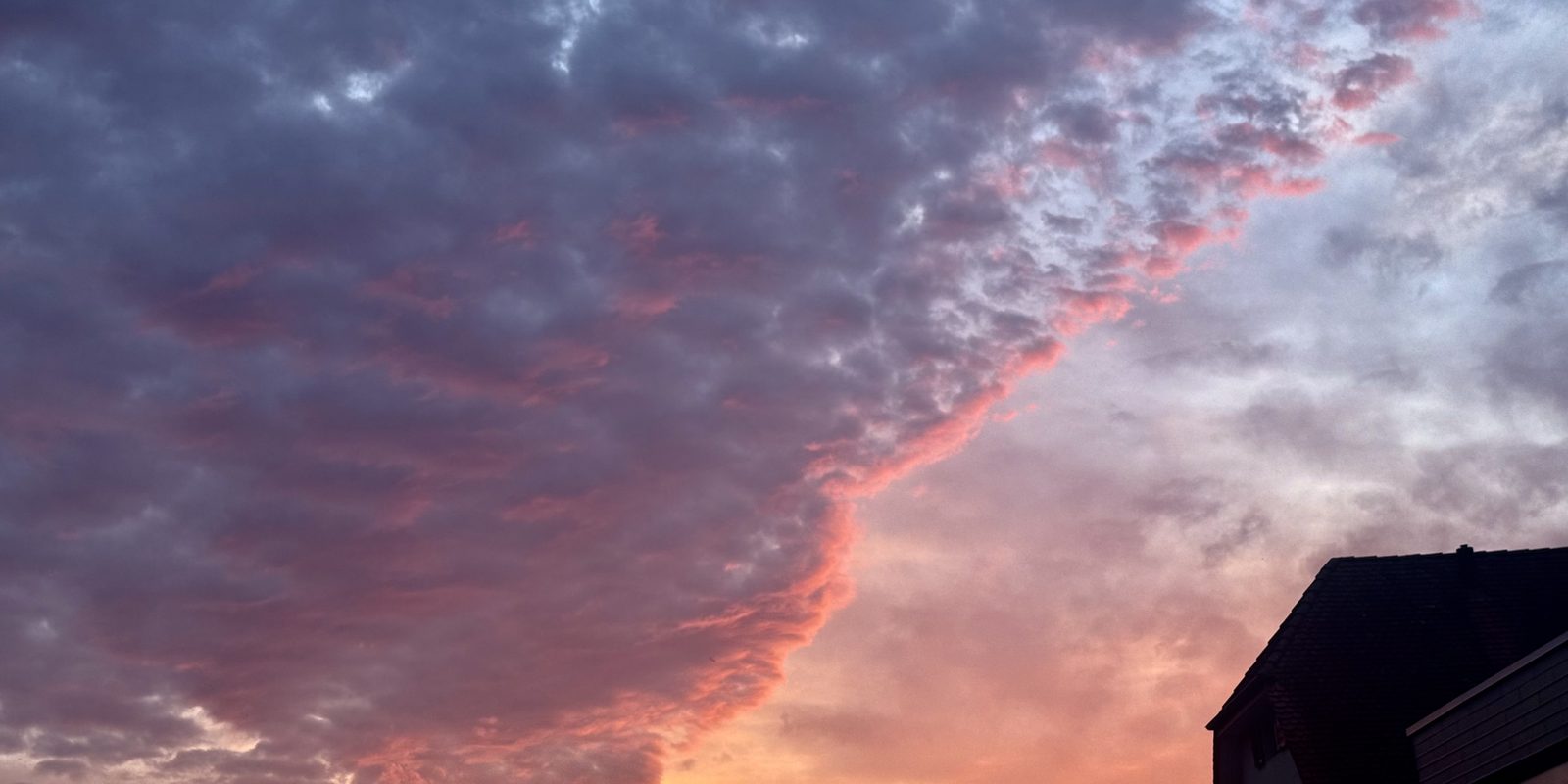 Rosa leuchtende Wolkenkante über einem Dach