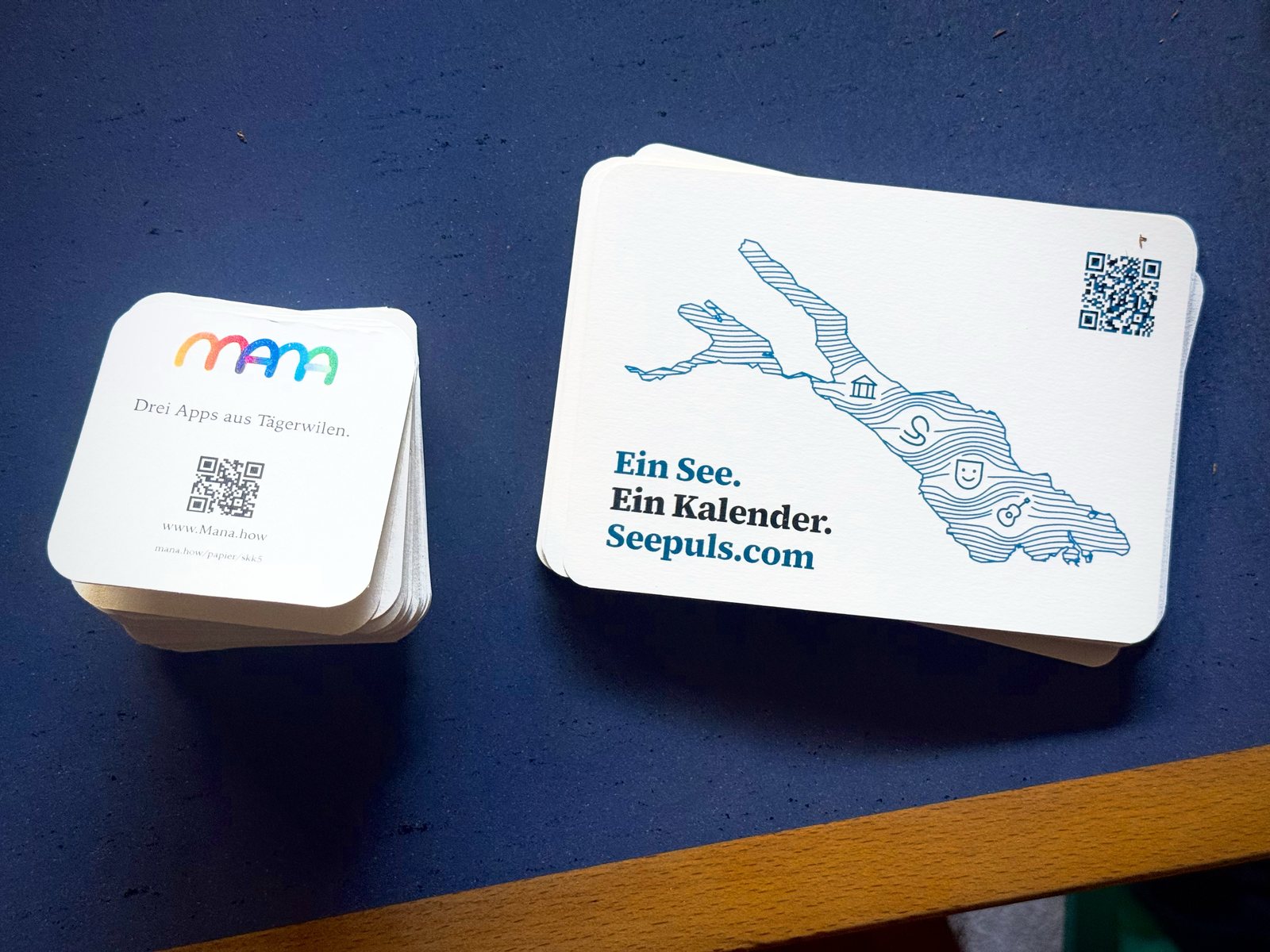 mana-Karten und Seepuls-Postkarten nebeneinander auf einem blauen Tisch